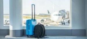 a blue suitcase and a backpack in front of an airplane